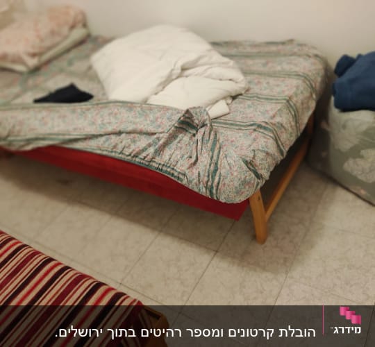 מיטה עם מצעים מקופלים ושק בגדים על הרצפה
